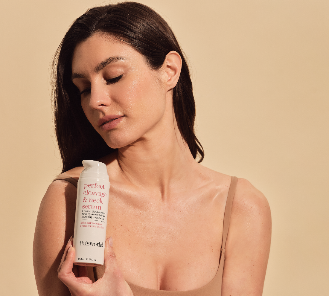 A woman holds thisworks perfect cleavage & neck serum against a warm beige background