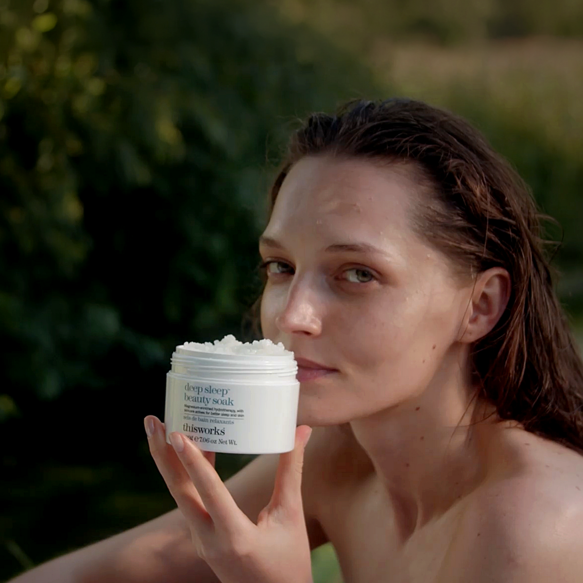 A woman outdoors holds a white jar of deep sleep beauty soak.