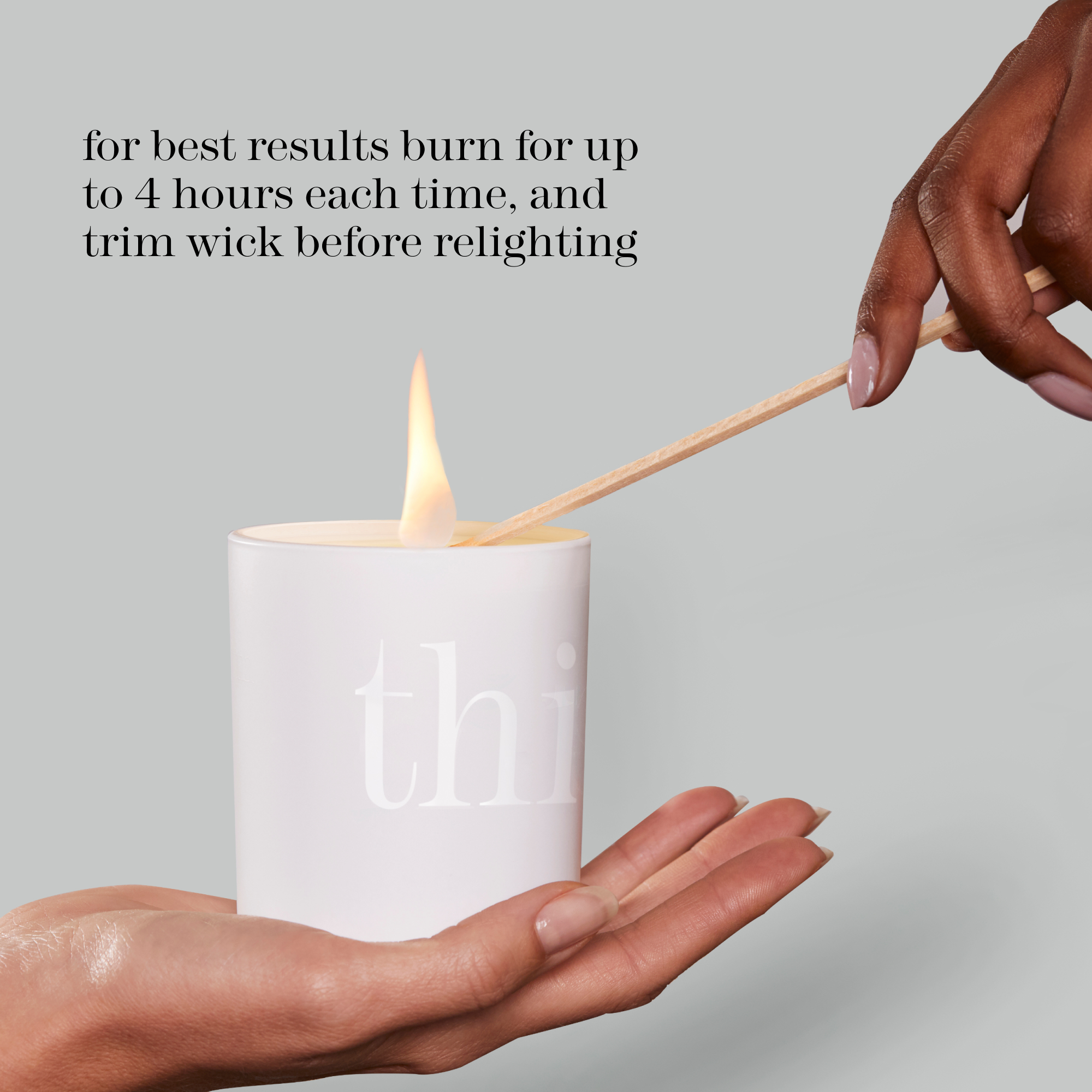 A white cylindrical candle with a visible flame is held in two hands, with a wooden matchstick resting across the top. Text on the image reads, 'for best results burn for up to 4 hours each time, and trim wick before relighting.